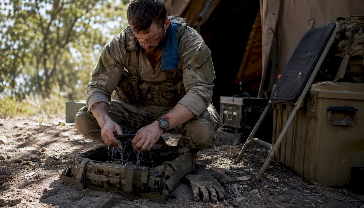 Soldier hand-washing socks outdoors using helmet liner basin